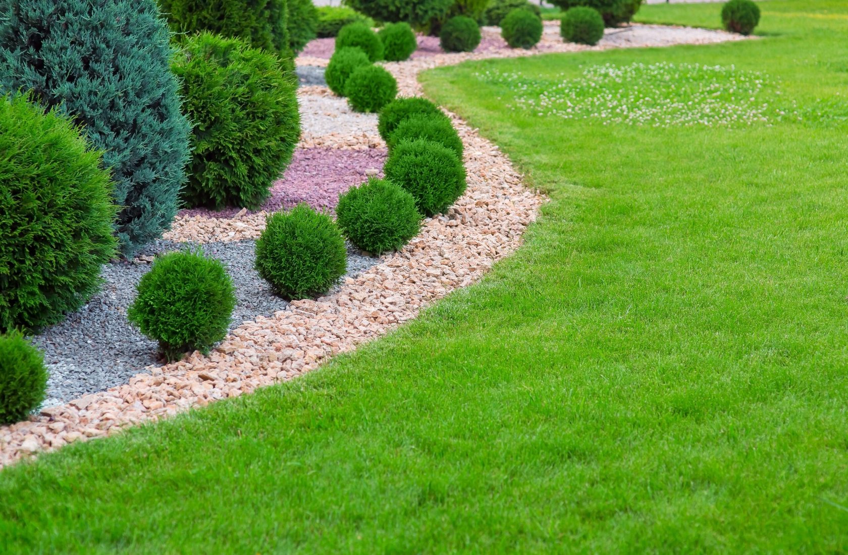 Landscape bed of garden with wave ornamental growth cypress bushes gravel mulch by color rock way on a day spring park with green lawn meadow, nobody. Landscape bed of garden with wave ornamental growth cypress bushes gravel mulch by color rock way on a day spring park with green lawn meadow, nobody.